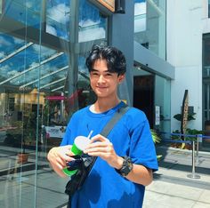 a young man holding a green and white object in his hand while standing next to a glass building