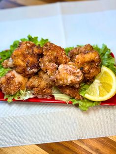 a red plate topped with meat and lettuce next to a slice of lemon