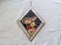 a stained glass sun catcher hanging on a white tablecloth with flowers in the window