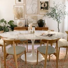 an oval marble table surrounded by chairs in a room with pictures on the wall and potted plants