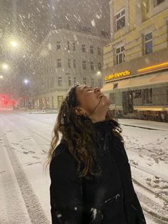 a woman standing in the middle of a snowy street with her eyes closed, looking up into the sky