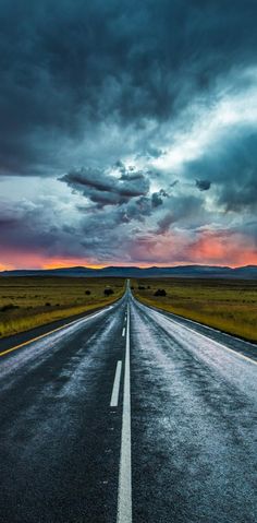 an empty road in the middle of nowhere under a cloudy sky with clouds above it