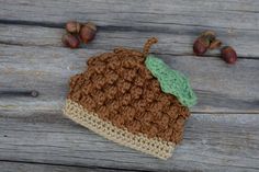 a crocheted hat sitting on top of a wooden table next to acorns