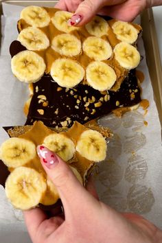 two hands reaching for peanut butter and banana slices on top of a chocolate cake in a box