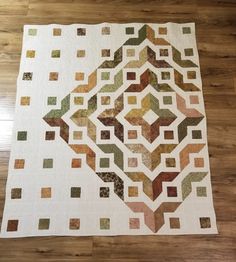 a white quilt with multicolored squares on the top and bottom, sitting on a wooden floor