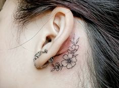 a close up of a person's ear with flowers behind the ear tattoo on their left side