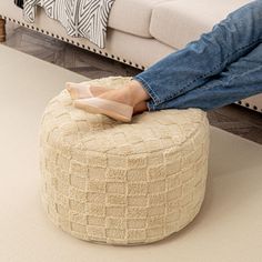 a person sitting on top of a foot stool in front of a couch with pillows