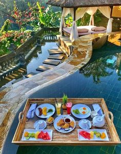 a tray with food and drinks on it next to a pool in the middle of a resort