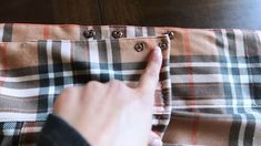 a person pointing to the side of a brown and white checkered bag with buttons on it