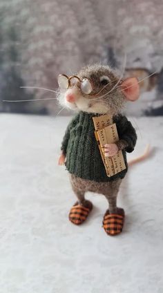 a toy mouse wearing glasses and a sweater holding a piece of paper in it's hand