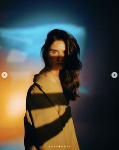 a woman with long hair standing in front of a colorful background and looking at the camera