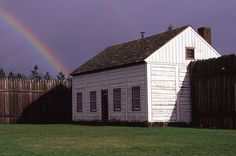 a white house with a rainbow in the sky above it and a wooden fence around it