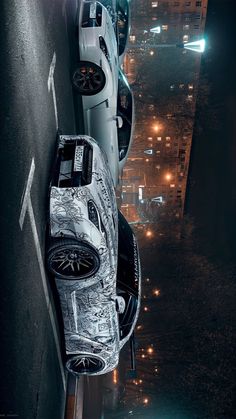 two cars parked next to each other on the side of a road at night with city lights in the background