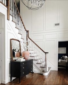 a living room with white walls and wooden floors, a chandelier and a mirror on the wall