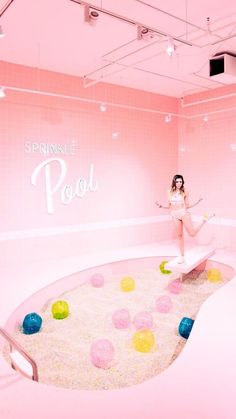 a woman is standing in a pink room with balls on the floor and an upside down pool