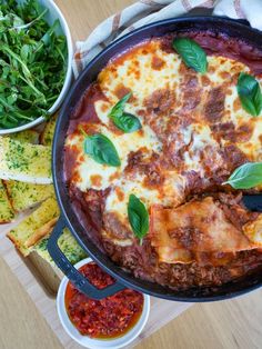 a pizza in a pan on top of a table next to bowls of salad and bread