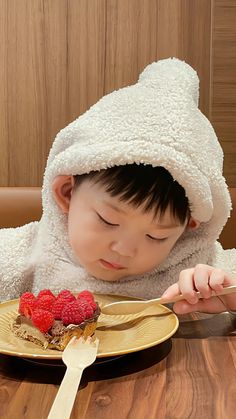 a young child in a bathrobe is eating some food on a plate with raspberries