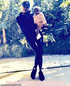 a woman holding a baby in her arms while standing on a wooden deck next to trees