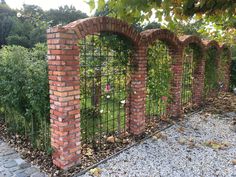 a brick fence is surrounded by plants and gravel