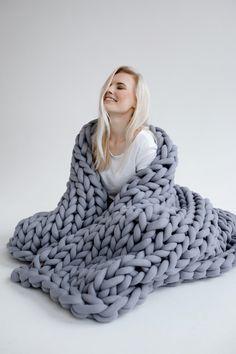 a woman sitting on the ground wrapped in a giant chunky blanket, with her eyes closed