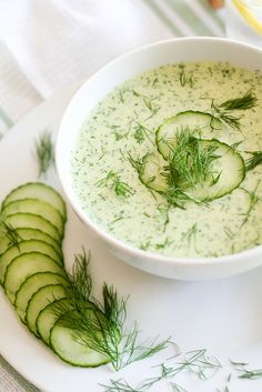 a bowl of soup with cucumbers and dill in it on a plate