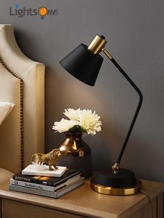 a table with a lamp, books and flowers on it next to a bed headboard