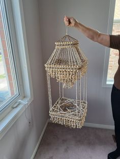 a woman is holding up a birdcage with beads on it in front of a window