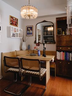 a dining room table with two chairs and a mirror on the wall above it, in front of a bookshelf