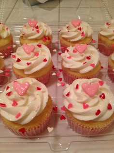 cupcakes with white frosting and pink hearts are on a clear plastic tray