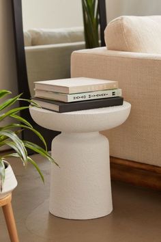 a stack of books sitting on top of a white pedestal next to a planter