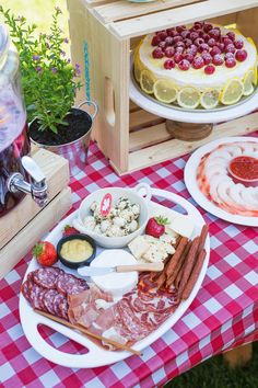 an assortment of cheeses, meats and fruit on a picnic table