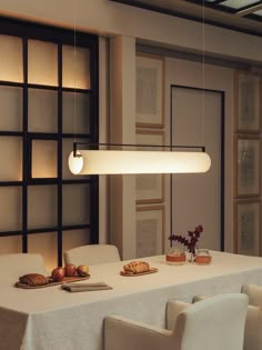 a dining room table with white chairs and an oval light fixture hanging over it's head