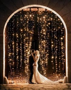 a bride and groom standing in front of an archway with lights on the wall behind them