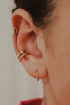 a woman wearing gold ear cuffs with two rings on her left side and one in the middle