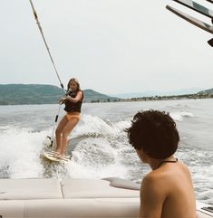 a woman on a wake board being pulled by a boat while another man watches from the water