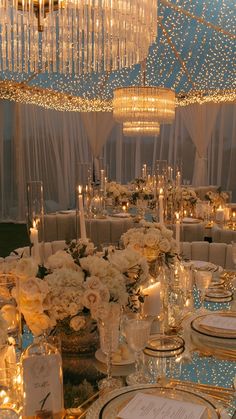 a table set up for a formal dinner with white flowers and candles on the tables