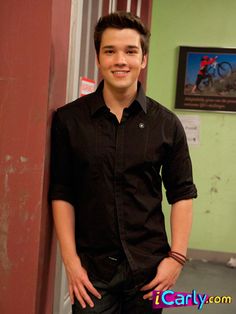 a young man standing next to a wall with his hands in his pockets and smiling at the camera