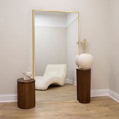 a large mirror sitting on top of a wooden floor next to two vases and a table