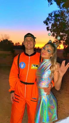 a man and woman dressed up in costumes standing next to each other with the sun setting behind them