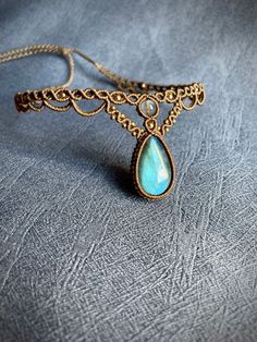 a gold necklace with a blue tear shaped stone on it's side, sitting on a gray surface