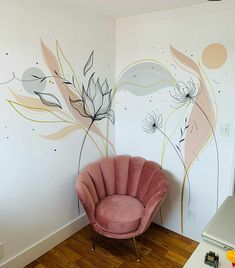 a pink chair sitting in front of a white wall with flowers painted on the walls