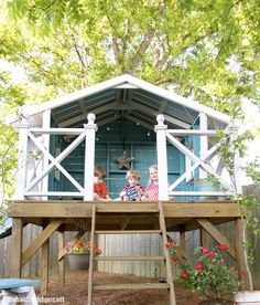 two children sitting on the top of a wooden platform in front of a blue house