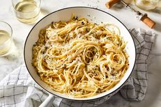 a white bowl filled with pasta next to two glasses of wine