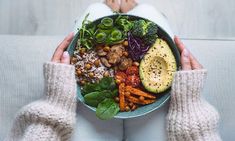 a person holding a bowl filled with vegetables and fruits in their hands while sitting on a couch