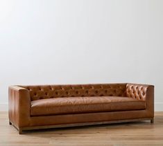 a brown leather couch sitting on top of a hard wood floor next to a white wall