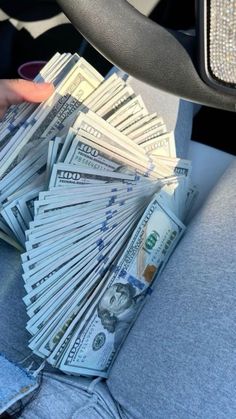 a pile of money sitting in the back seat of a car next to someone's hand