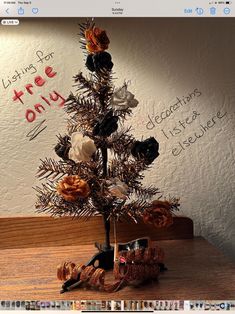 a small christmas tree decorated with flowers and ribbons on top of a wooden table in front of a white wall