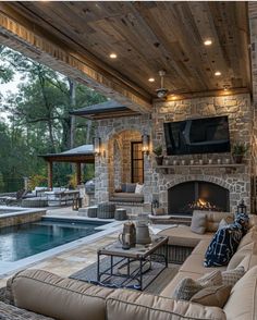 an outdoor living area with fireplace, couches and television on the wall next to a swimming pool