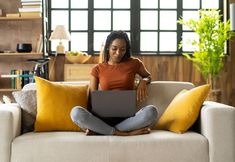 a woman sitting on a couch with her laptop in front of her and looking at the screen