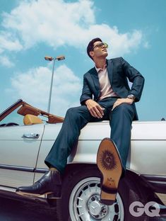 a man sitting on top of a white car with his feet up in the air